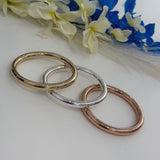 Three gold, silver, and rose gold bracelets on a white surface with flowers in the background.