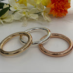 Three gold bracelets on a white surface with flowers in the background