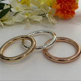 Three gold bracelets on a white surface with flowers in the background