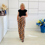 Woman wearing a black top and patterned pants standing in a room with decorative elements.