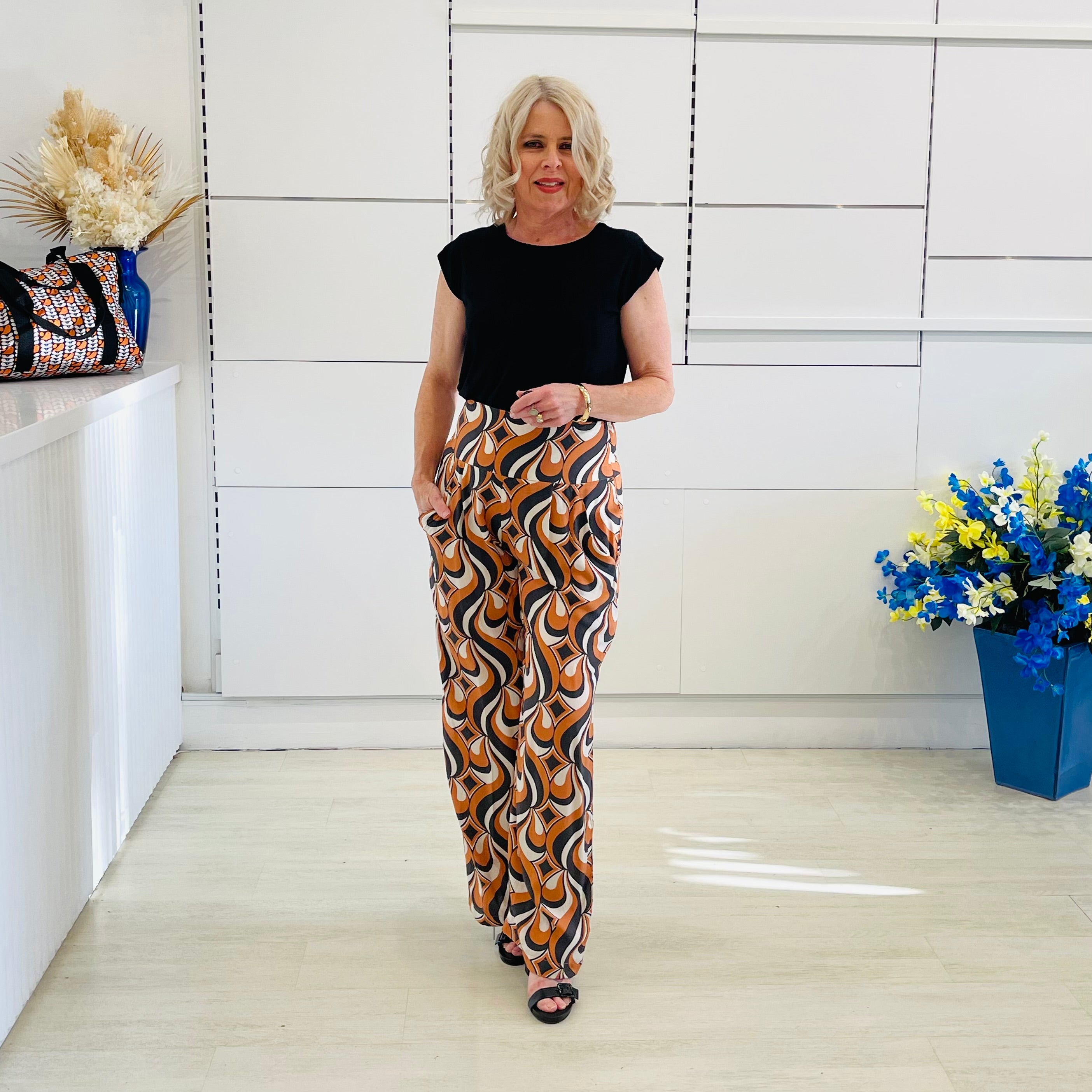 Woman wearing a black top and patterned pants standing in a room with decorative elements.