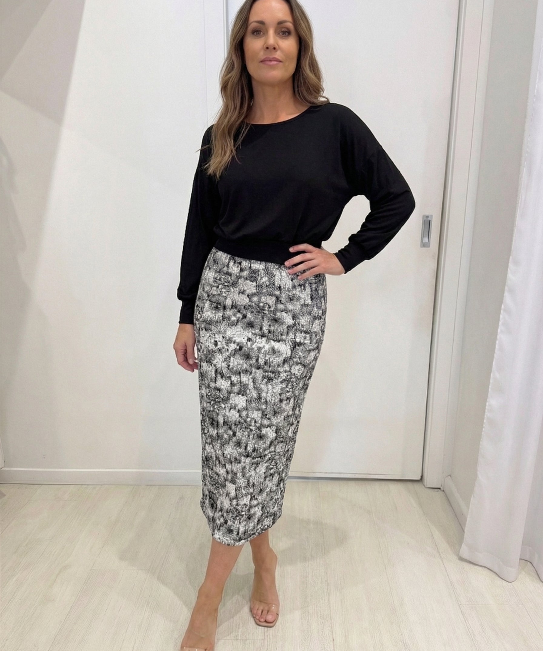 Woman wearing a black top and patterned skirt in a minimal indoor setting