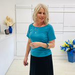 Woman in a teal green dressy top standing in a room with white walls and decorative elements.