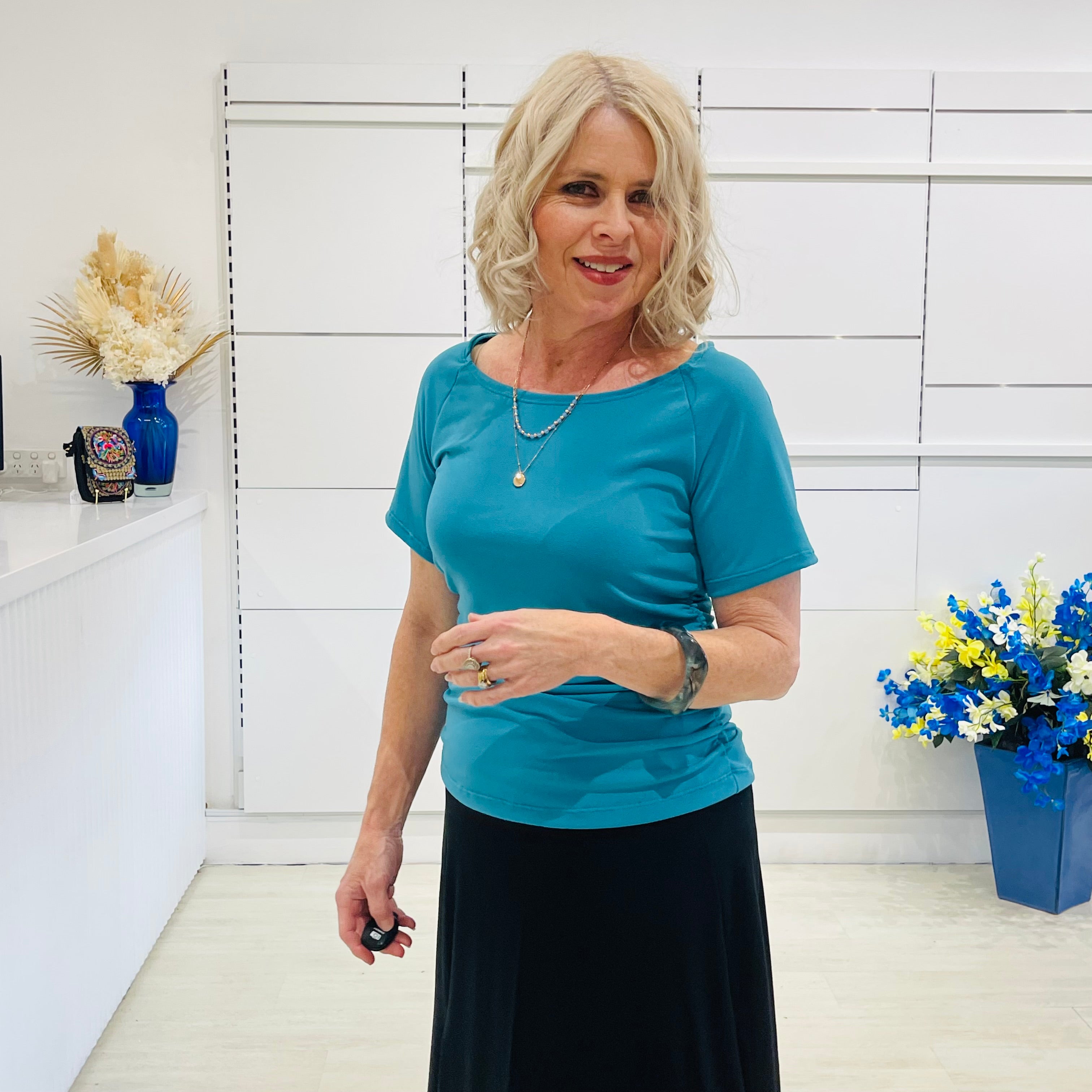 Woman in a teal green dressy top standing in a room with white walls and decorative elements.