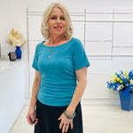 Woman wearing a blue top standing in a room with white walls and decorative elements.