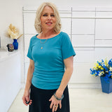 Woman wearing a blue top standing in a room with white walls and decorative elements.