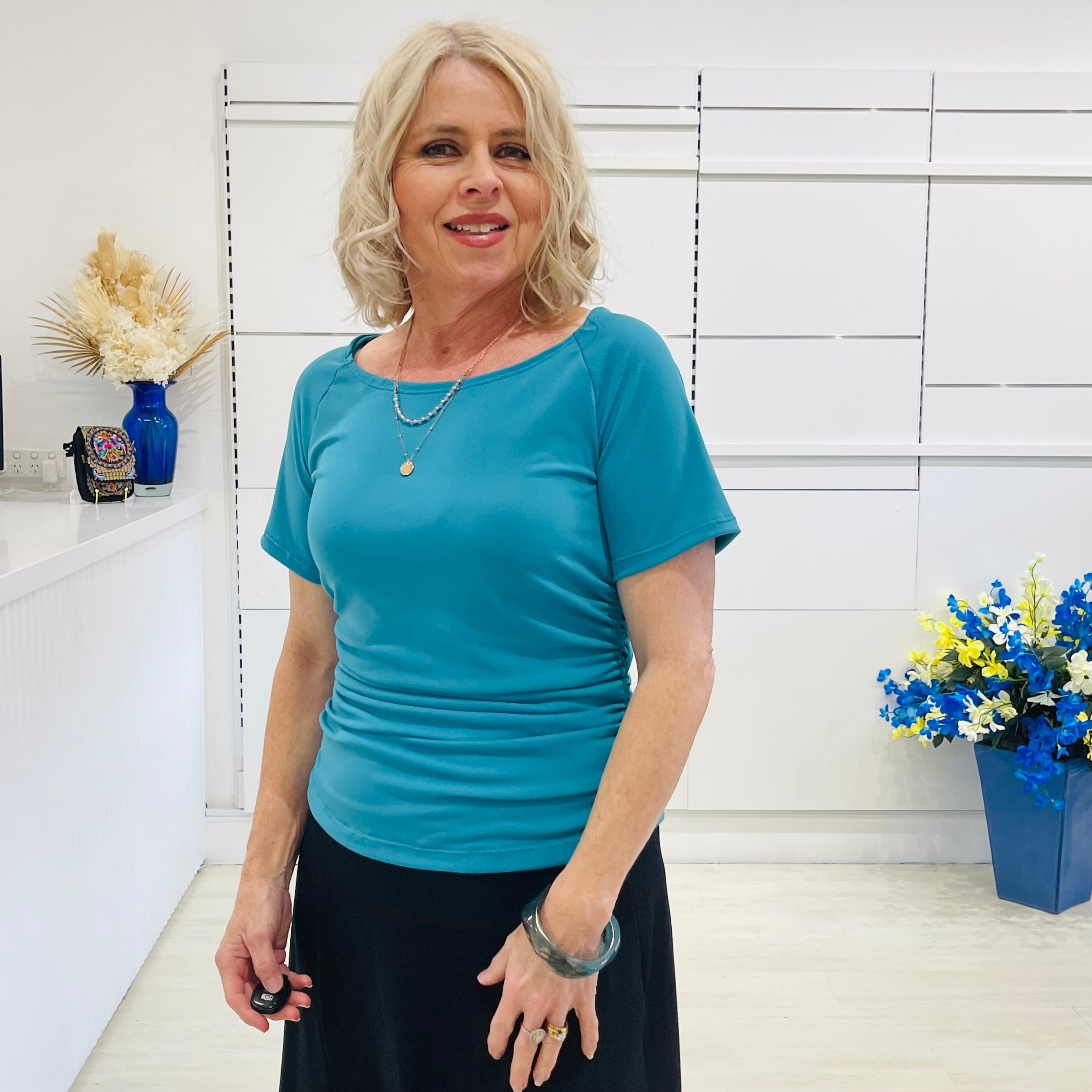 Woman wearing a blue top standing in a room with white walls and decorative elements.
