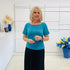 Woman in a green shirt and black skirt standing in a room with white walls and decorative elements.