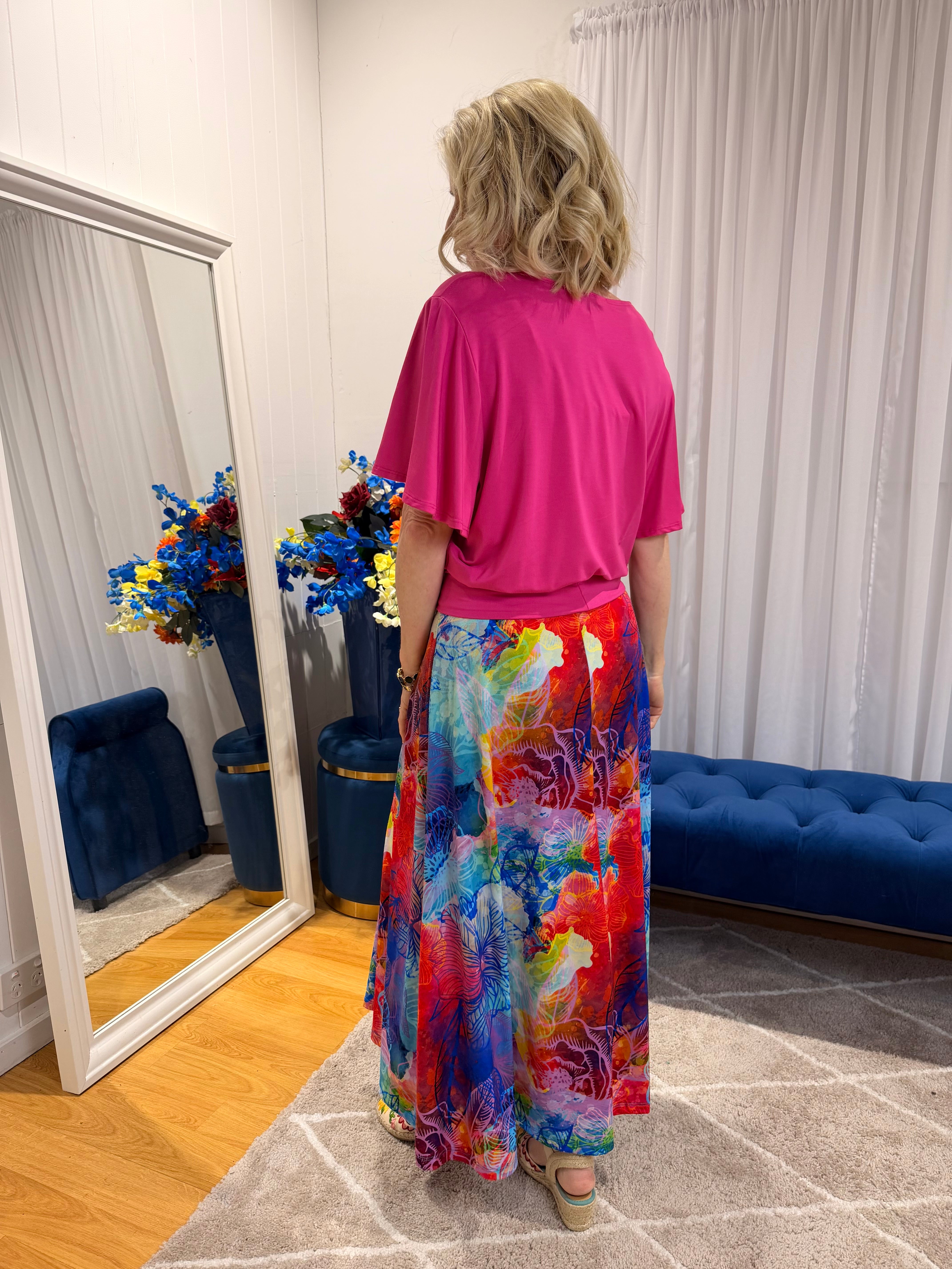 Woman wearing pink short sleeve top and colourful skirt.