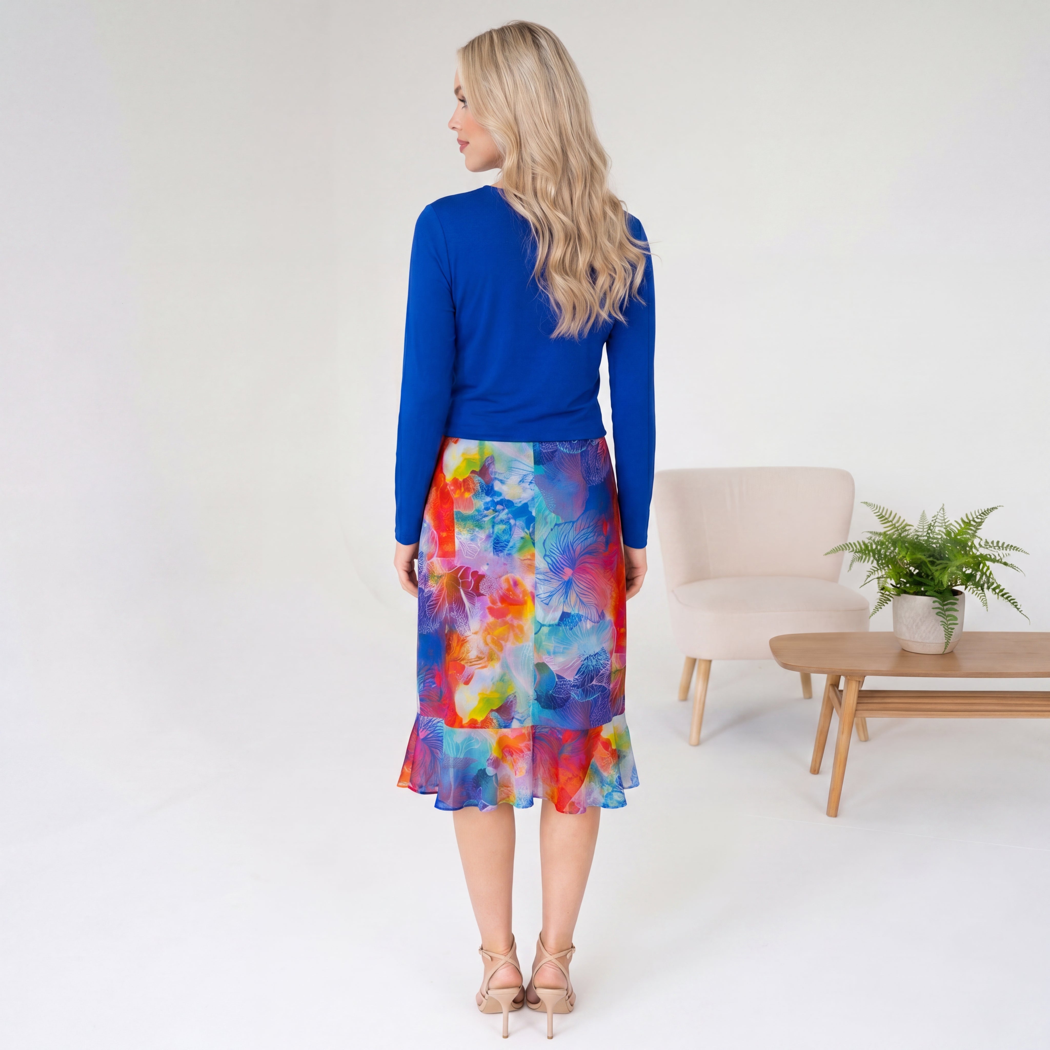 Woman wearing a blue top and colorful skirt in a minimalistic room.