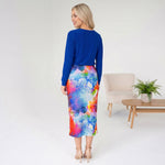 Woman wearing a blue top and colorful skirt in a minimalistic room.