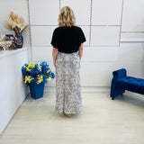Woman standing in a room with a white wall, blue bench, and floral arrangement.