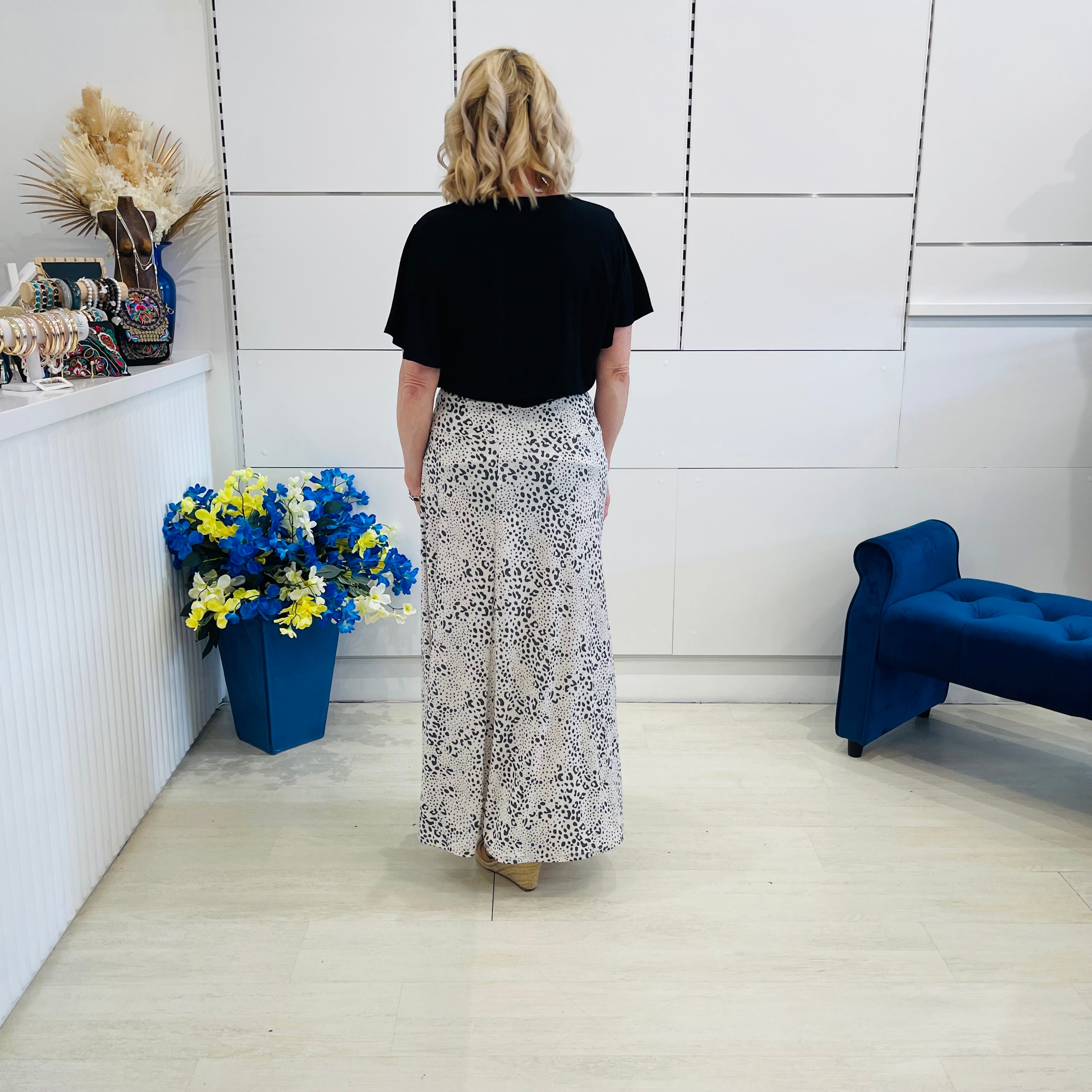 Woman standing in a room with a white wall, blue bench, and floral arrangement.