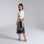 Woman wearing a white top and patterned skirt on a plain background