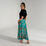 Woman wearing a black top and teal floral skirt on a plain background