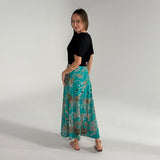 Woman wearing a black top and teal floral skirt on a plain background