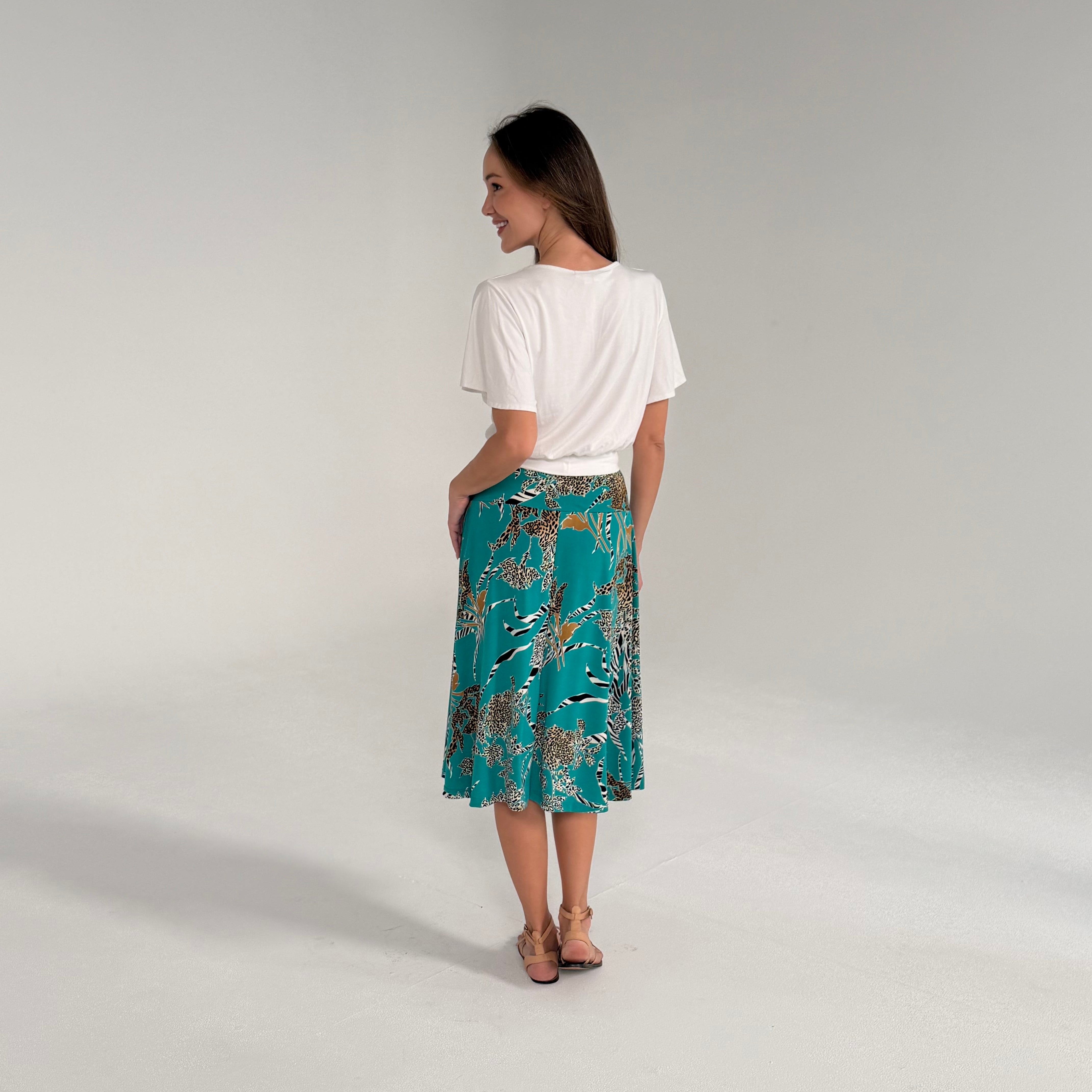 Woman wearing a white top and teal patterned skirt on a plain background