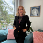 Woman in a black suit standing in a living room with pink cushions and a scenic view.