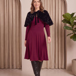 Woman wearing a burgundy dress with a black fur shrug in a neutral setting