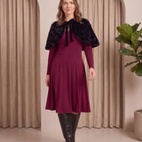 Woman wearing a burgundy dress with a black fur shrug in a neutral setting