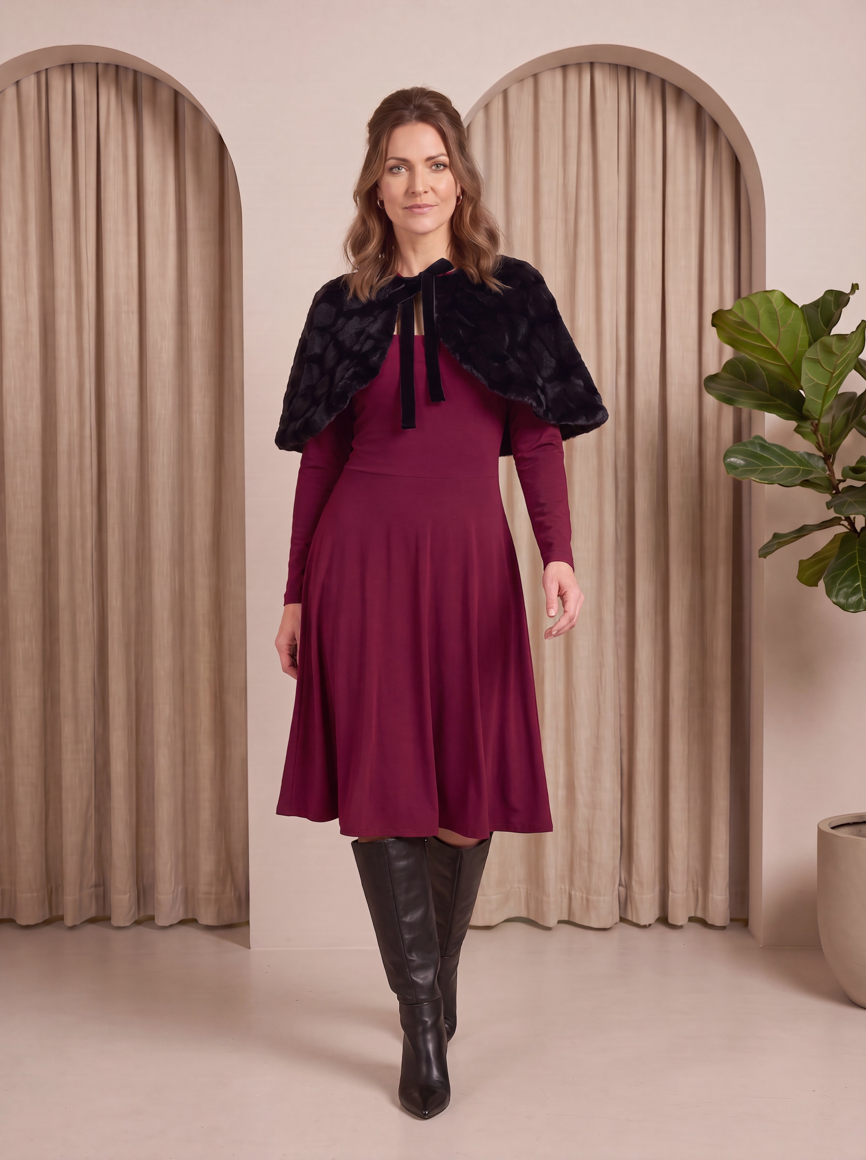 Woman wearing a burgundy dress with a black fur shrug in a neutral setting