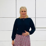 Woman in black top and printed skirt standing in a white room 