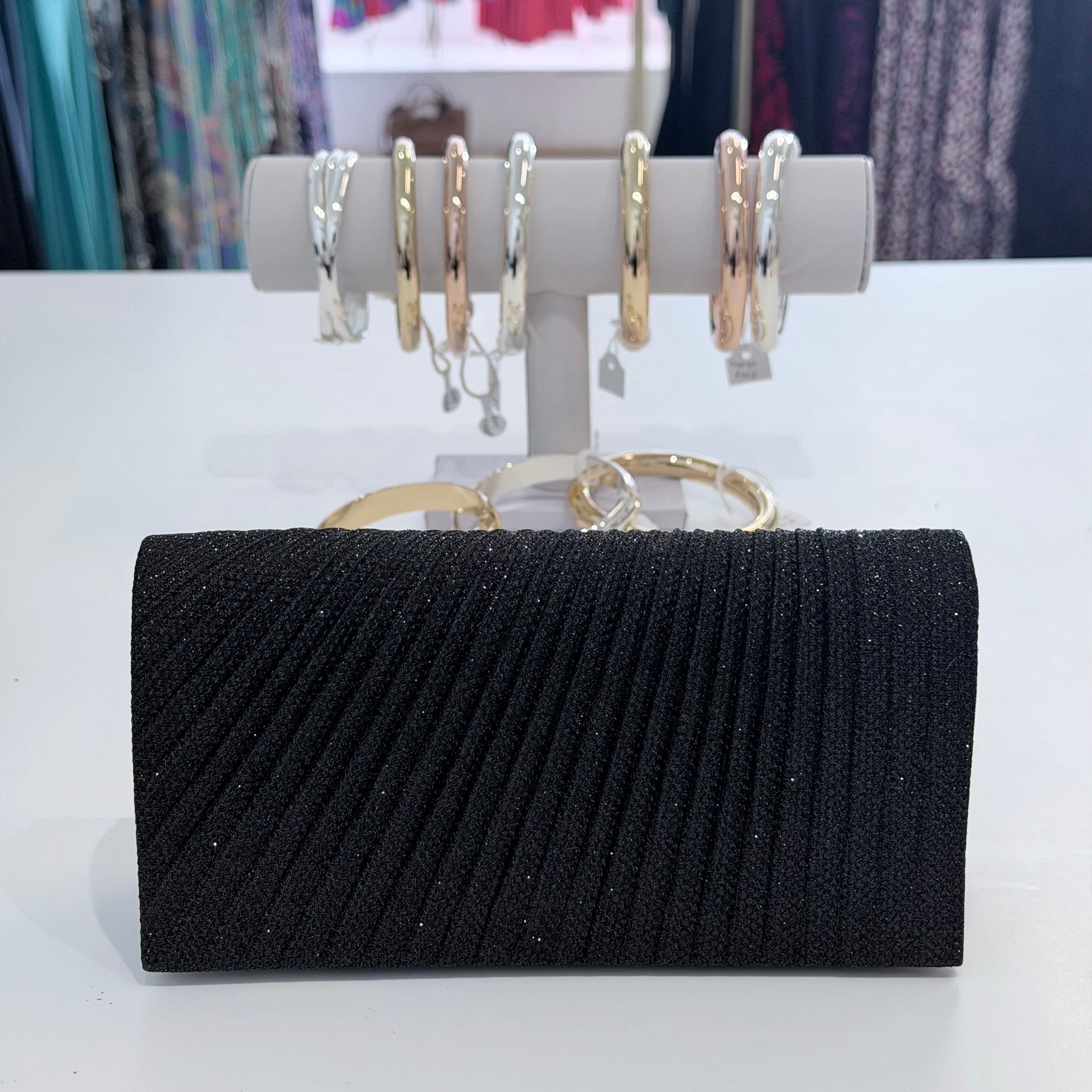 Black clutch bag with a jewelry stand featuring rings and bracelets on a white surface.