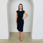 Woman wearing a black dress standing in a white archway.
