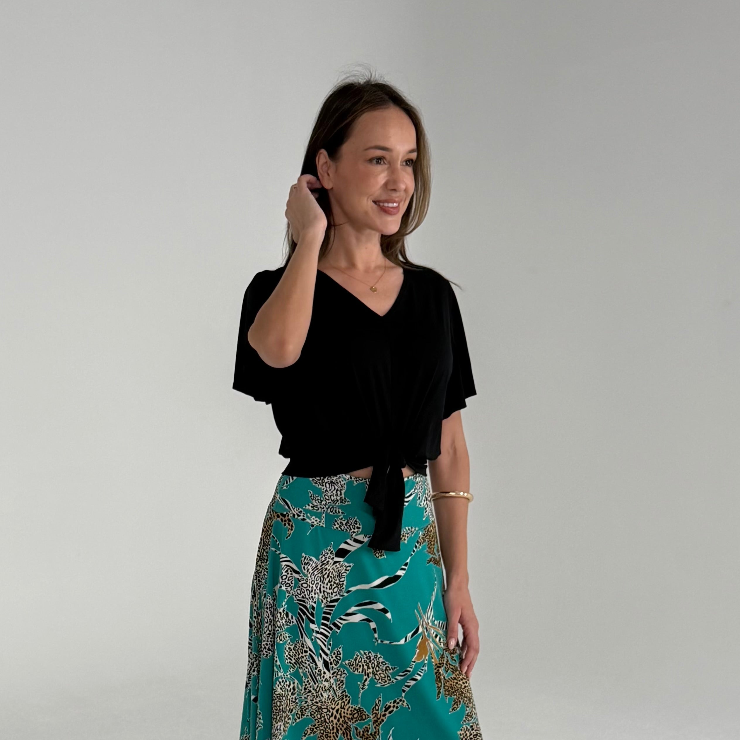 Woman wearing a black top and teal patterned skirt against a plain background