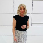 Woman wearing a black top and patterned skirt against a white tiled wall