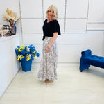 Woman standing in a modern room with a blue flower arrangement and a blue chair.