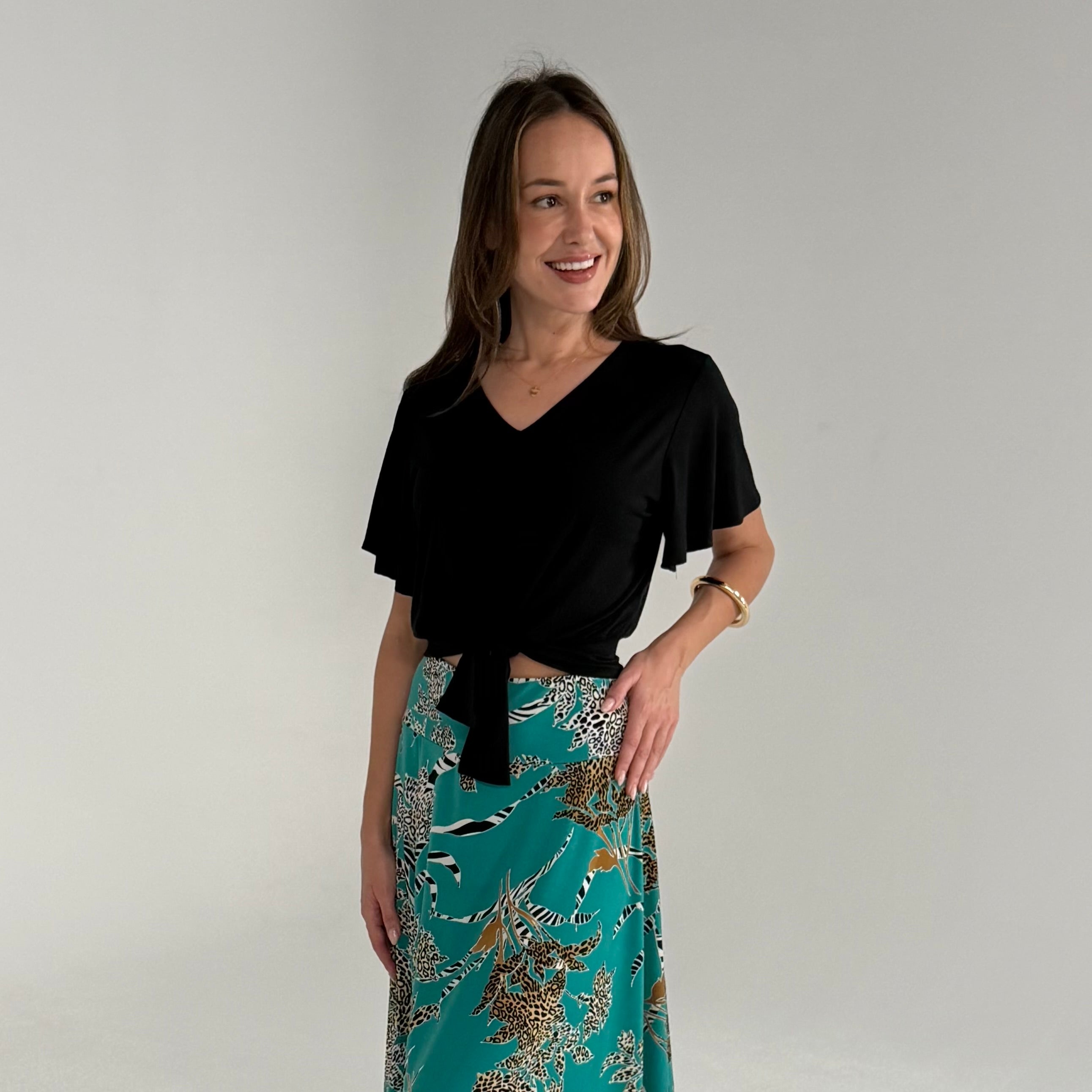 Woman wearing a black top and a teal patterned skirt against a plain background