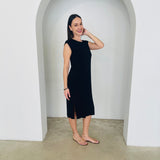 Woman wearing a black sleeveless dress standing in a white archway.