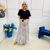 Woman standing in a room with a white wall, blue chair, and flower arrangement.