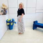 Woman standing in a modern interior setting with a blue flower arrangement and a blue chair.