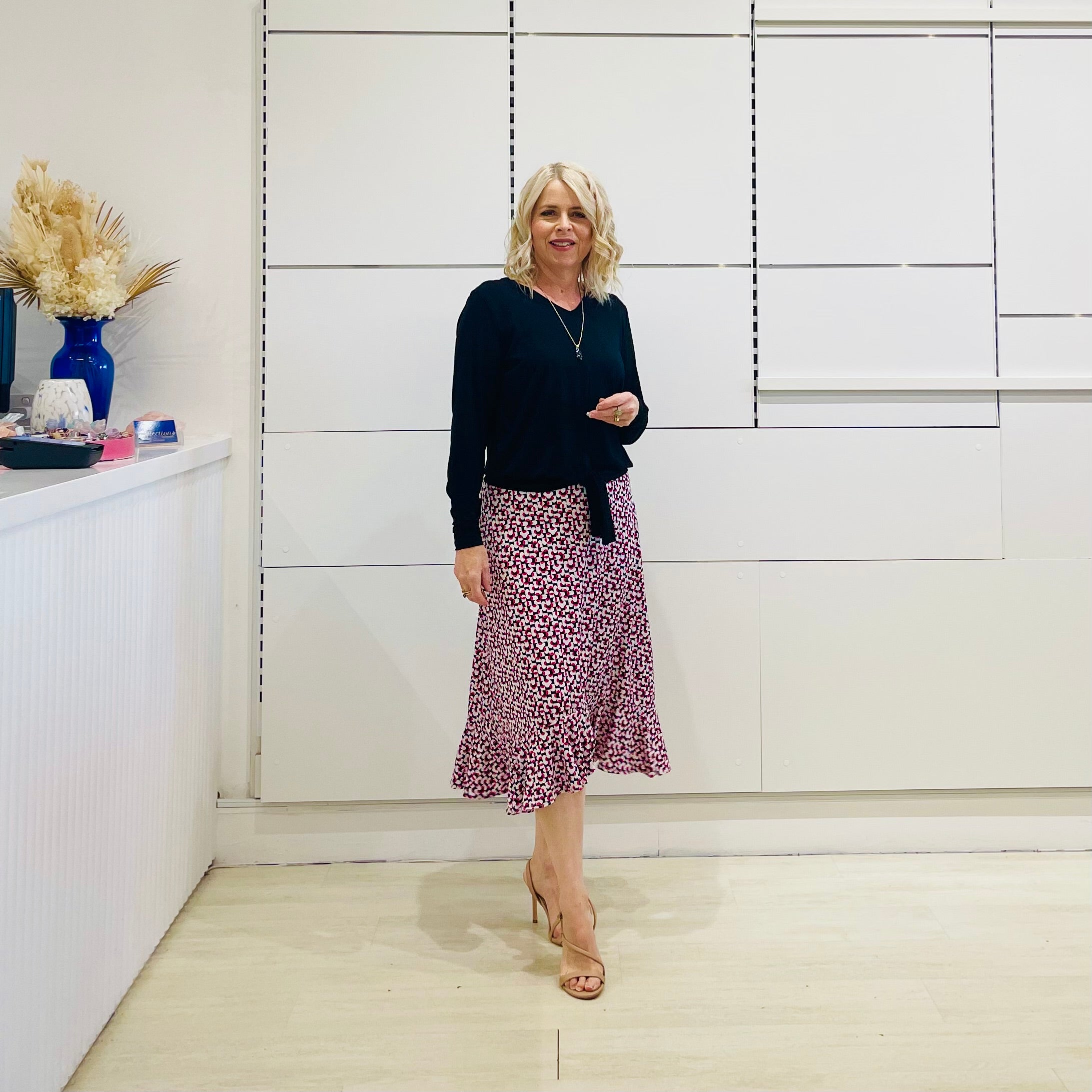 Relaxed fit, black bamboo, v neckline, long sleeve, tie front detail, dressy top. Worn with midi length skirt with slight hemline ruffle in black,white and pink. 