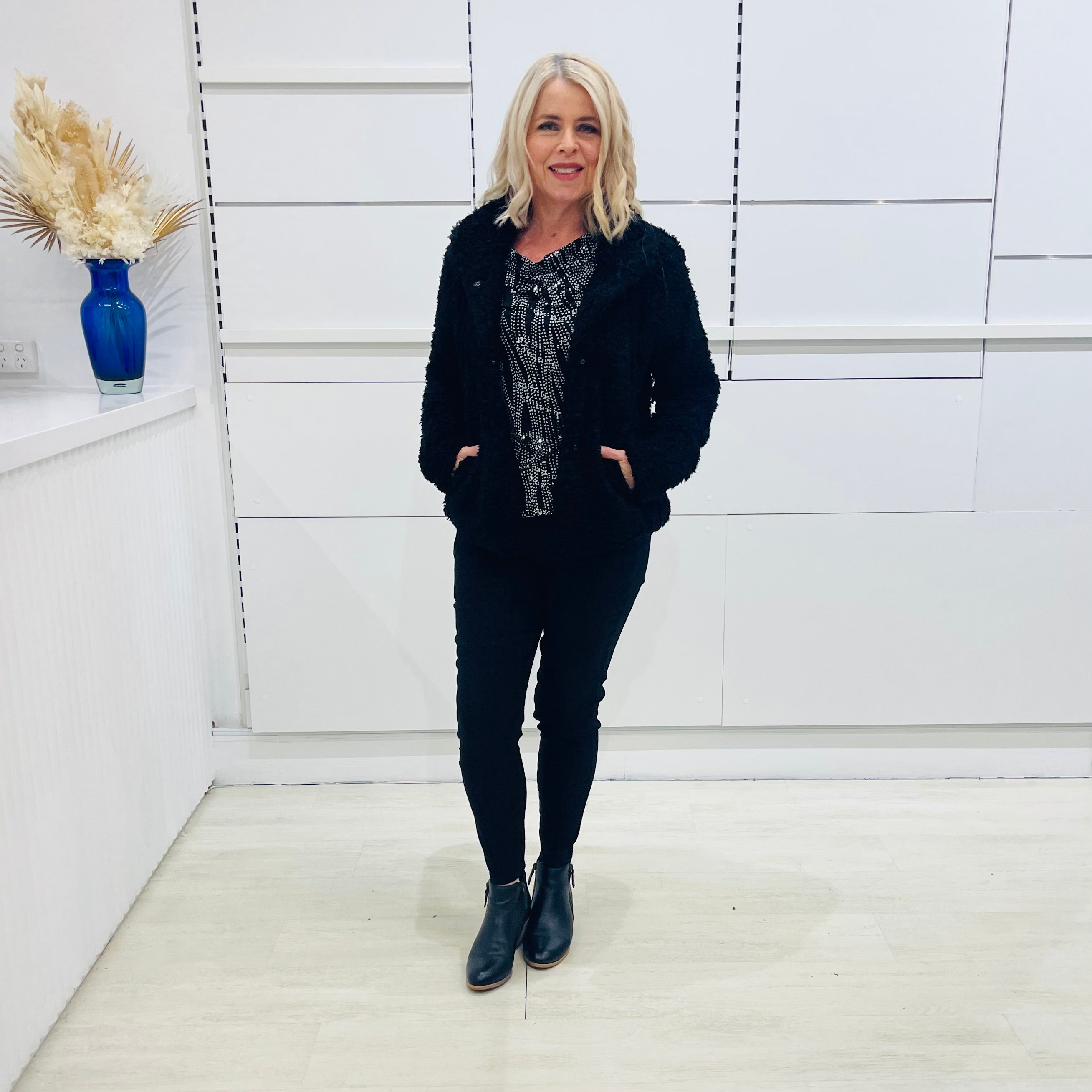 Black fluffy, faux fur, teddy bear jacket with pockets. Worn with black tailored fitted pants and a black and silver sparkly cowl neckline top. 