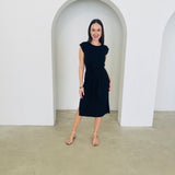 Woman in a black dress standing in front of white arches.