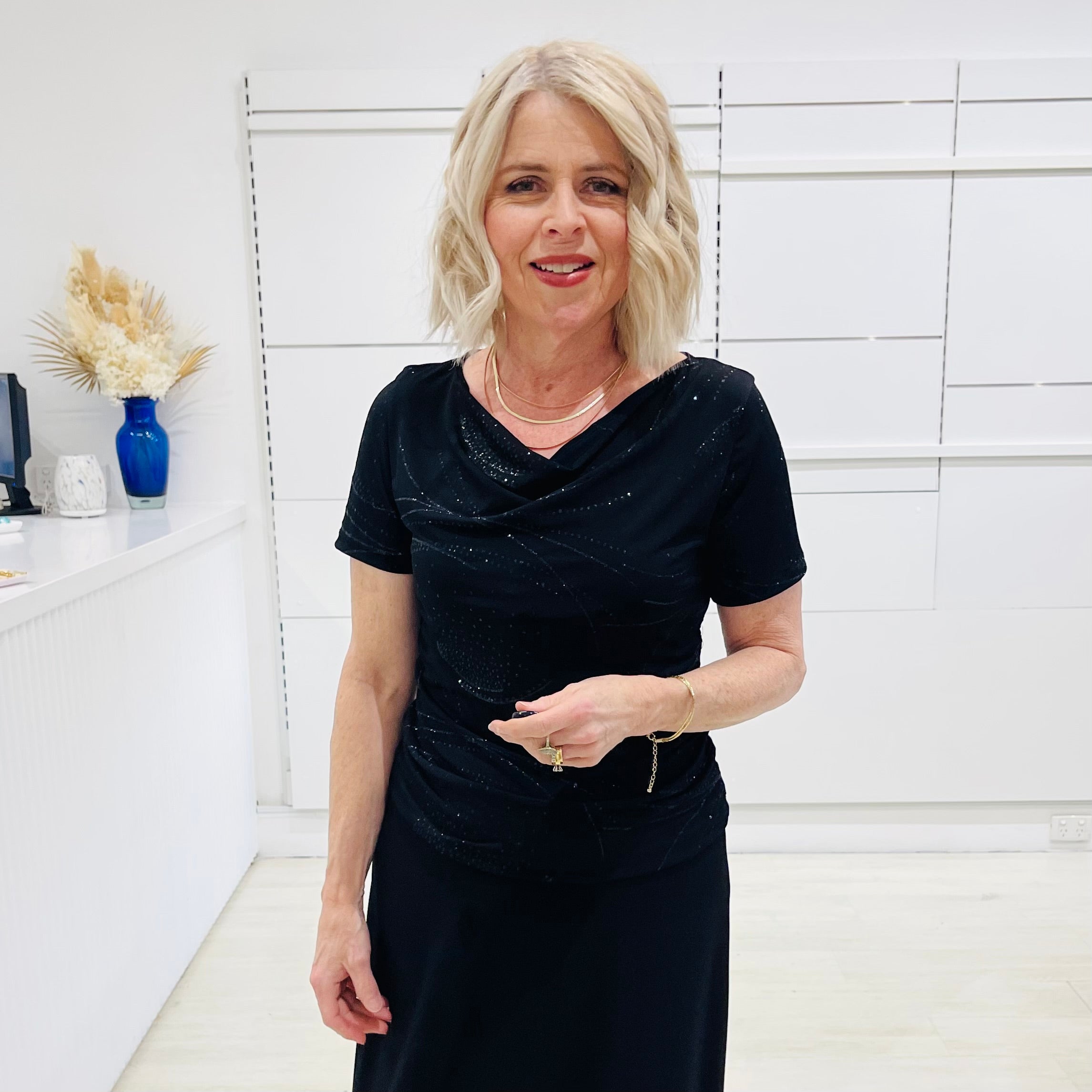 Woman in a black dress standing in a room with white walls and decorative elements.
