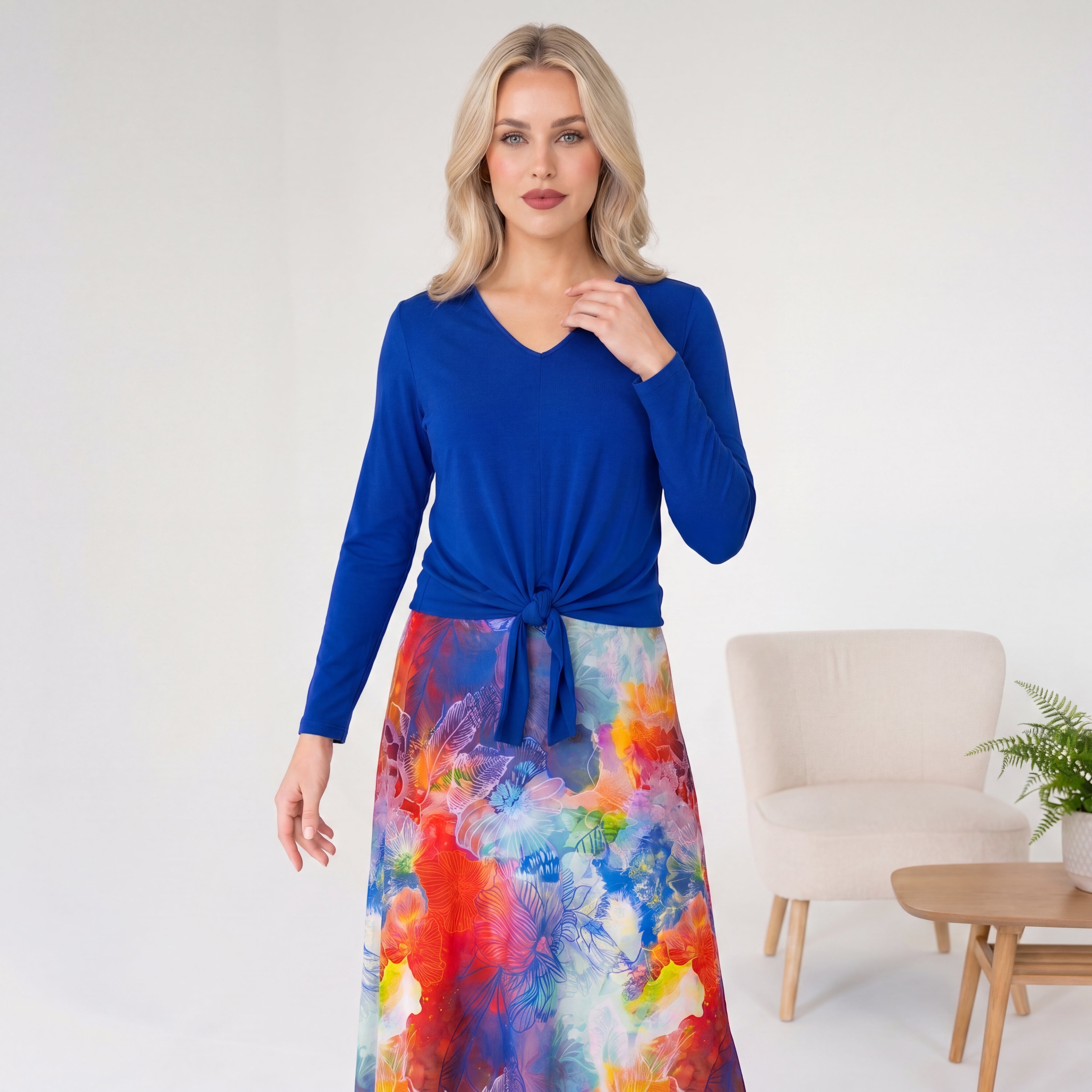 Woman wearing a blue top and colorful skirt in a minimalistic room.