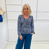 Woman wearing a long sleeve, semi fitted, flowy blue top with a delicate leaf print, paired with denim blue colored linen pants.