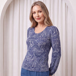 Woman wearing a blue patterned top and pants against a white curtain background