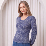 Woman wearing a blue patterned top and pants against a white curtain background