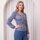 Woman wearing a blue patterned top and pants against a white curtain background