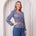 Woman wearing a blue patterned top and pants against a white curtain background