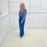 Woman wearing a flowy, long sleeve, scoop necklin, blue top with a delicate leaf print, paired with denim blue colored linen pants.