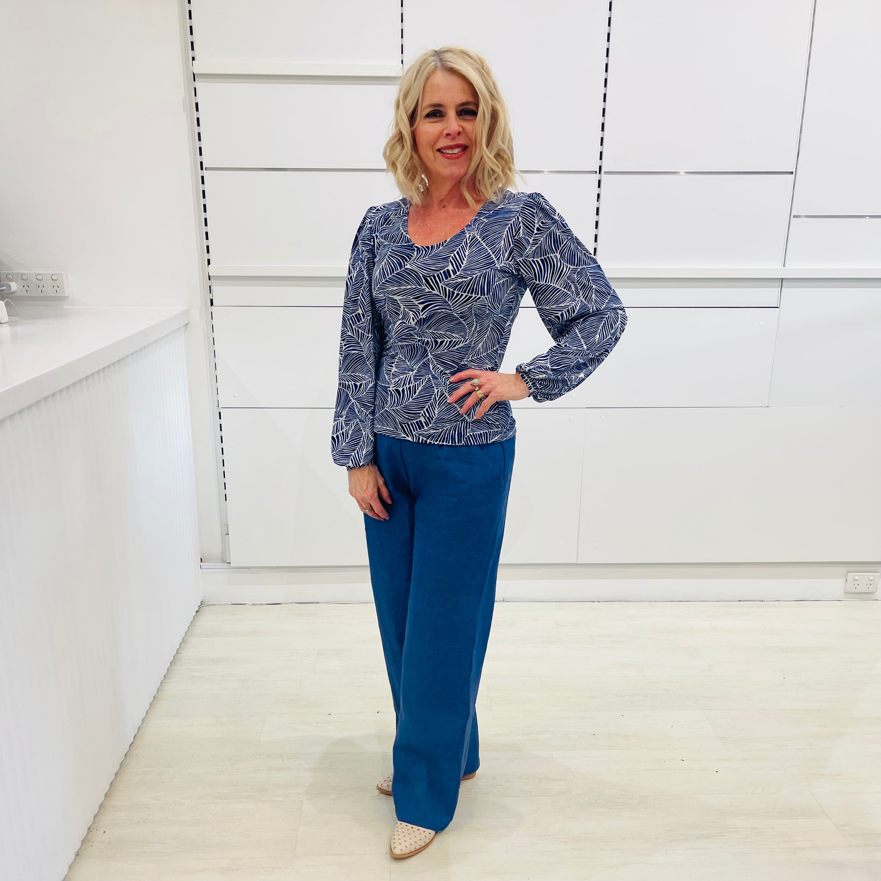 Woman wearing a flowy blue top with a delicate leaf print, paired with denim blue colored linen pants.