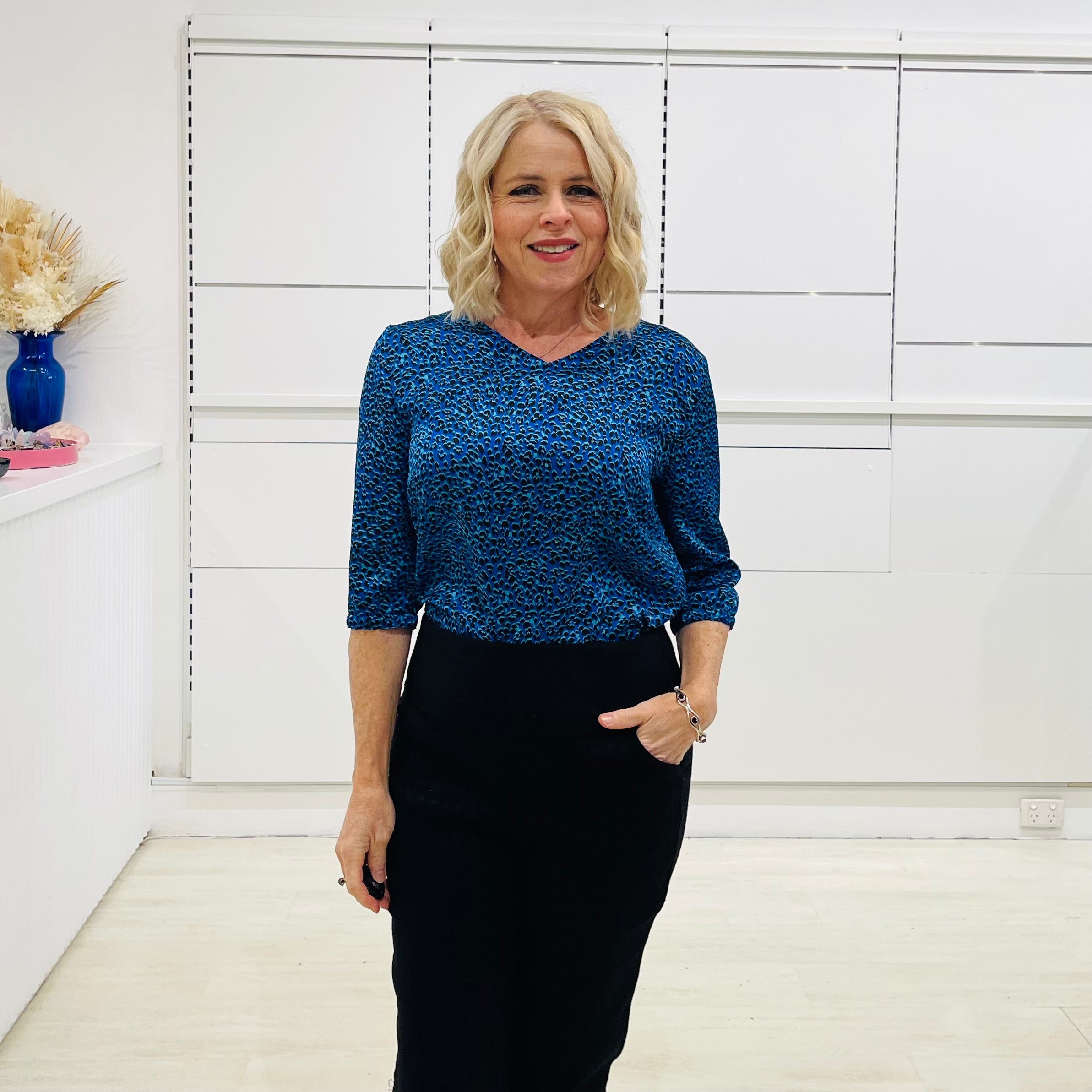 Stylish v- neck, three quarter sleeve blouse in a vibrant blue and black leopard print, paired with high-waisted black pants. A chic and polished look perfect for work or a smart casual outing