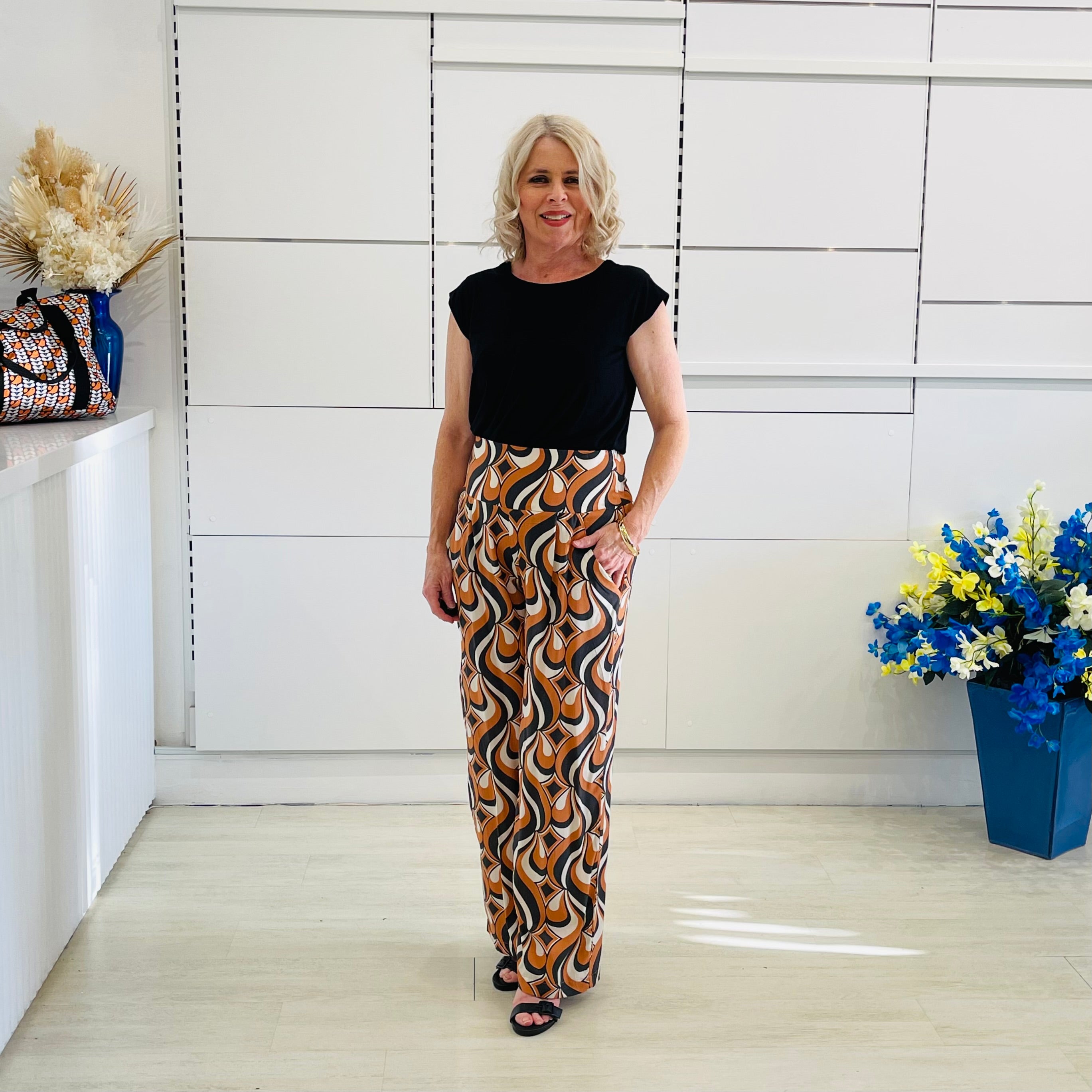 Woman in black top and patterned pants standing in a room with white walls and decorative elements.