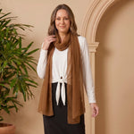 Woman wearing a brown scarf standing next to a potted plant against a beige wall.